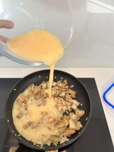 Pouring beaten eggs over potatoes and onion in non-stick pan